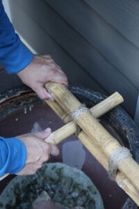 man holding bamboo pieces in place while wrapping twine over zip ties and around the…